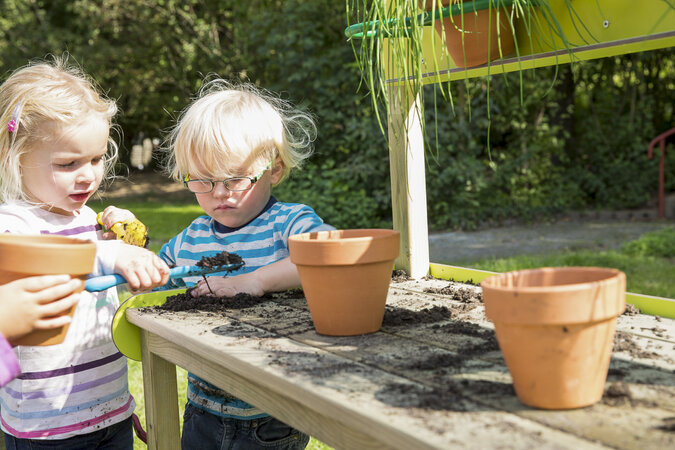 Speeltoestel voor kinderopvang van eibe - twee kinderen planten bloempotten op een houten bank.
