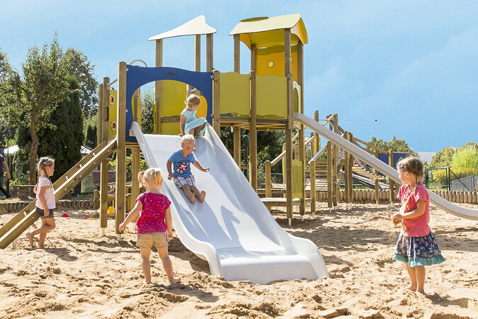 Speeltoestel voor kinderopvang van eibe - kleurrijke speeltuin met spelende kinderen op een grote zandvlakte.